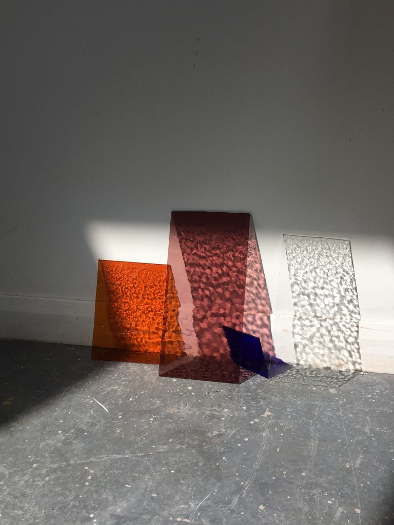Textured and coloured glass leans against a wall with light creating interesting shadows
