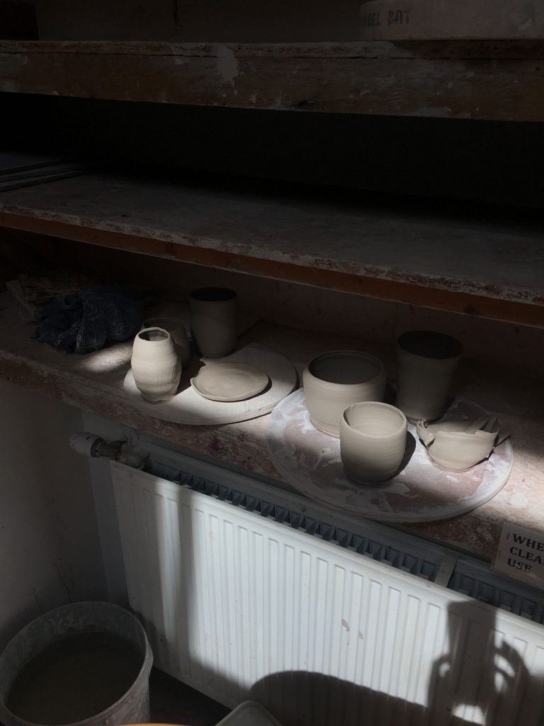 newly thrown ceramic pots sit in a beam of light on a shelf in the ceramics studio