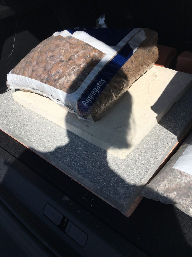 supplies from the builders merchants in the boot of a car; a stack of stone slabs and a bag of gravel with the word 'aggregates'