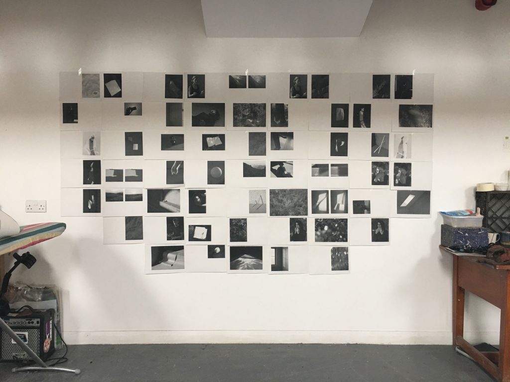 black and white photocopies of photographs laid out on a wall between a desk and an ironing board