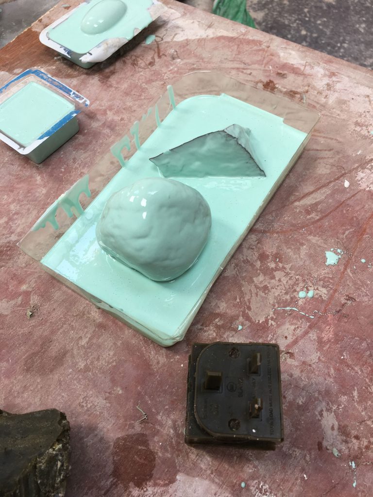 experiments with bright turquoise latex in the studio.  A dark green wax cast of an electrical adaptor sits in the foreground. 