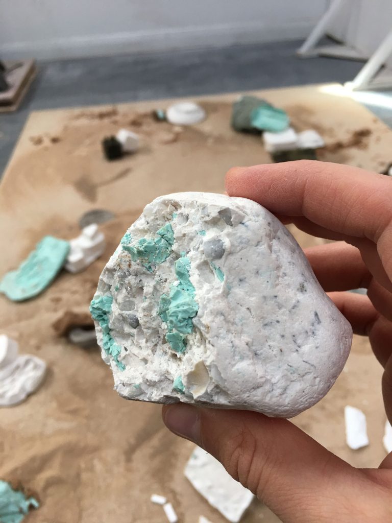 a hand holds a white stone with turquoise latex bits roughly attached