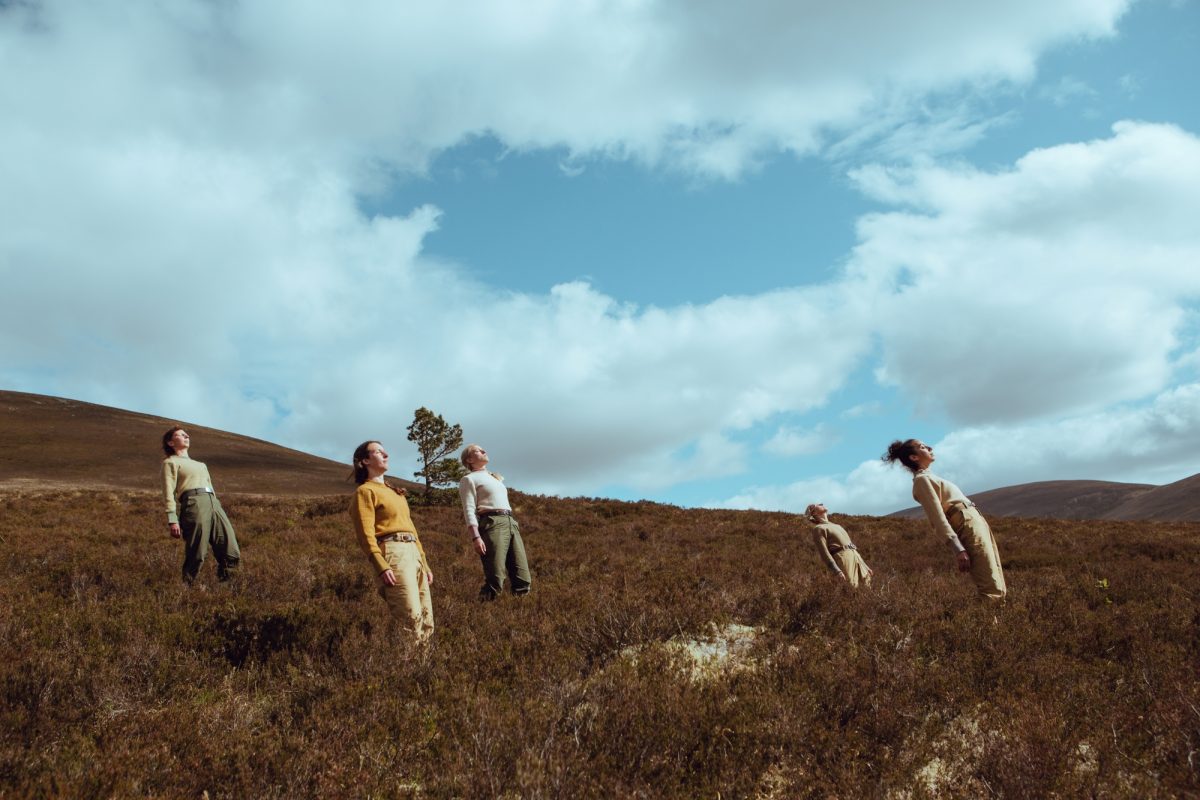 five dancers lean to look at the sky on a heather covered hillside