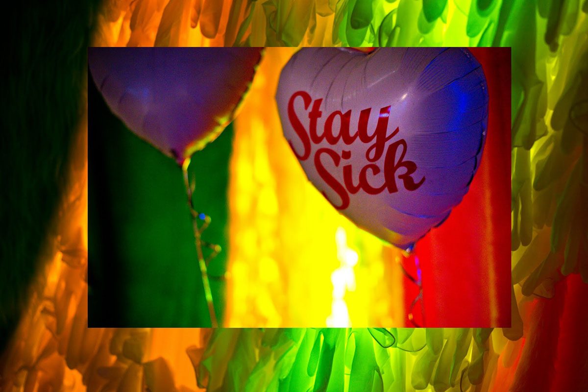 A heart shaped helium balloon with the words 'stay sick' on a brightly coloured and lit background