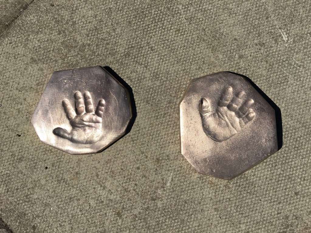 Two oblong bronze plates with a relief of a child's hand on concrete slabs. 