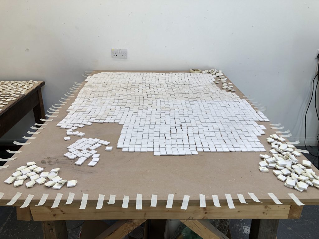 a workbench covered in a grid of small white tiles, small strips of masking tape are stuck all the way around the edge of the bench