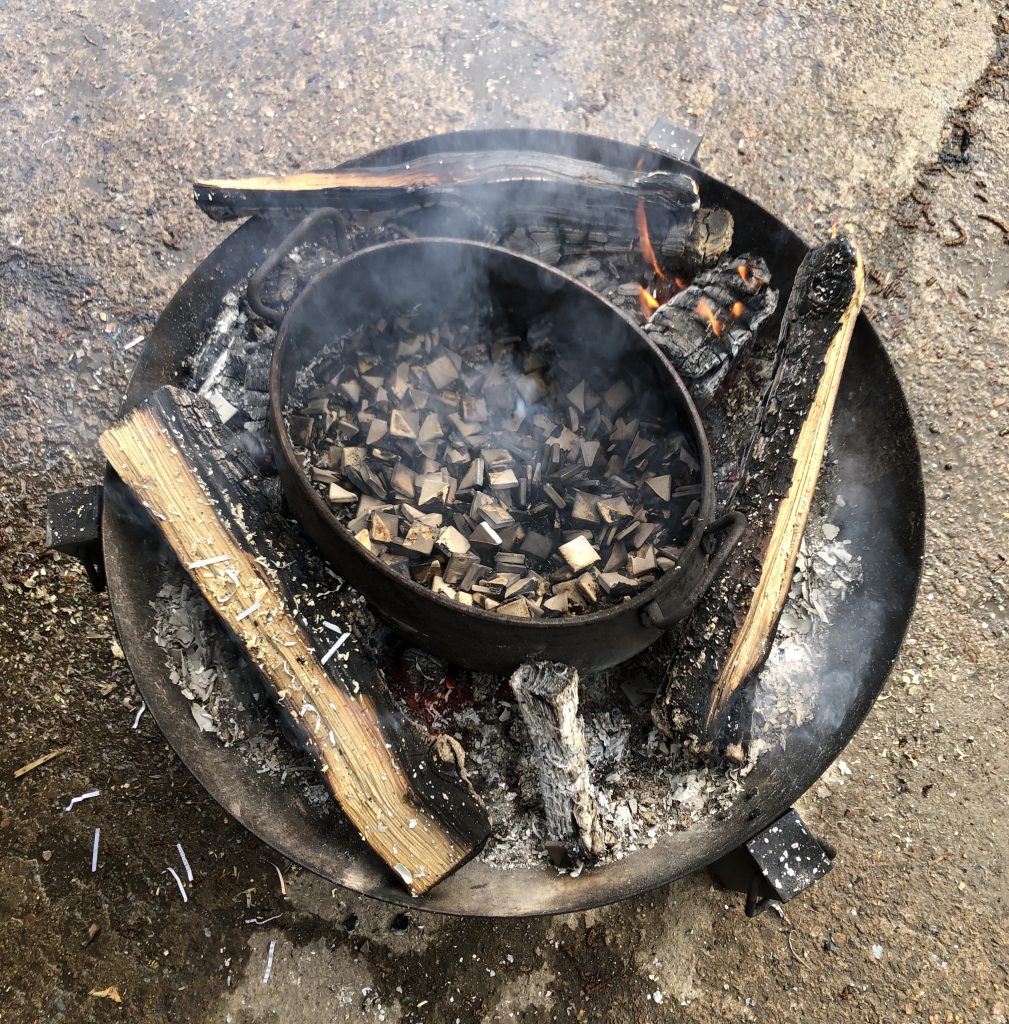 a smoky pit firing with a metal pot filled with small tiles